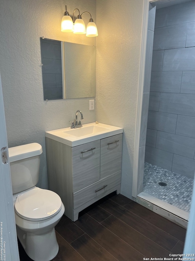 bathroom with large vanity, toilet, and tiled shower