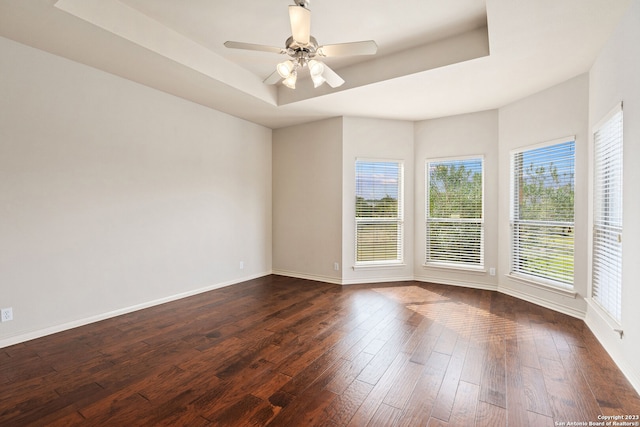 empty room featuring dark hardwood / wood-style floors, ceiling fan, and a tray ceiling