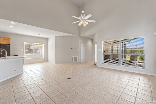 unfurnished living room featuring ceiling fan with notable chandelier, a healthy amount of sunlight, high vaulted ceiling, and light tile floors