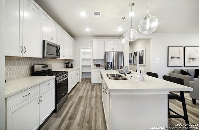 kitchen featuring pendant lighting, stainless steel appliances, a kitchen island with sink, white cabinets, and a sink