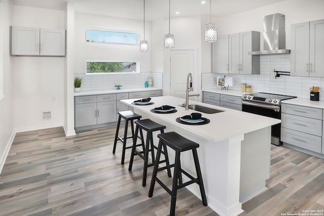 kitchen featuring wall chimney range hood, backsplash, stainless steel range with electric stovetop, and sink