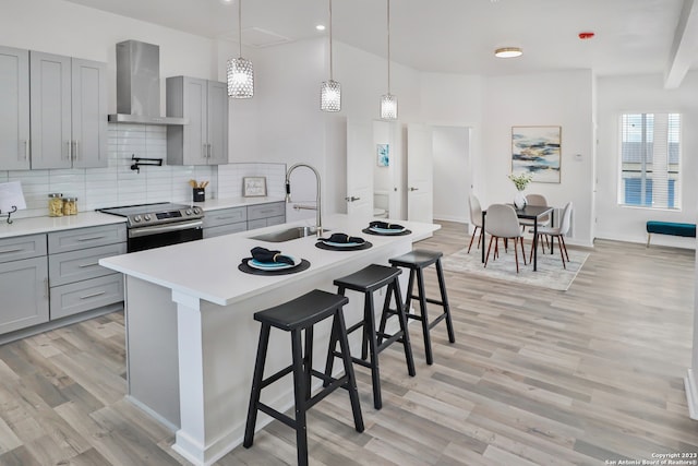 kitchen featuring stainless steel range with electric cooktop, wall chimney range hood, sink, and light wood-type flooring