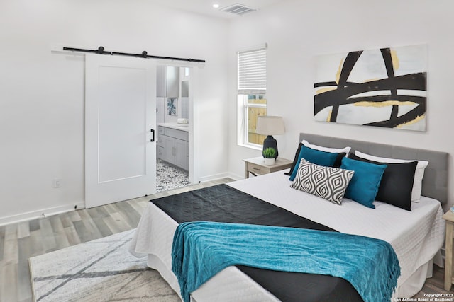 bedroom with a barn door, ensuite bathroom, and light hardwood / wood-style flooring