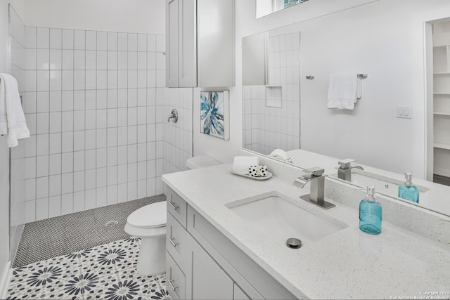 bathroom with tile floors, toilet, a tile shower, and vanity