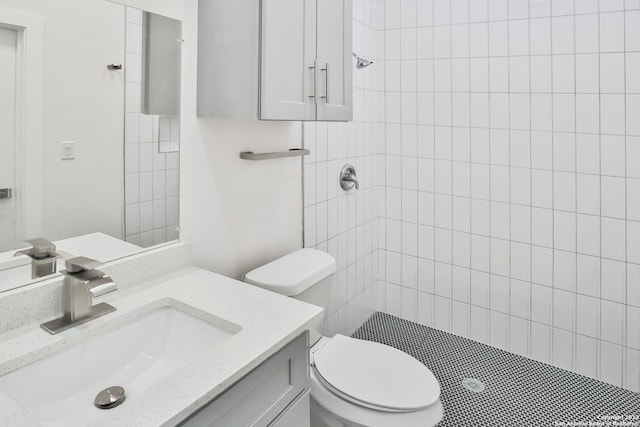 bathroom with toilet, a tile shower, and vanity