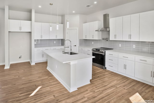 kitchen featuring wall chimney range hood, electric range, white cabinetry, a kitchen island with sink, and sink