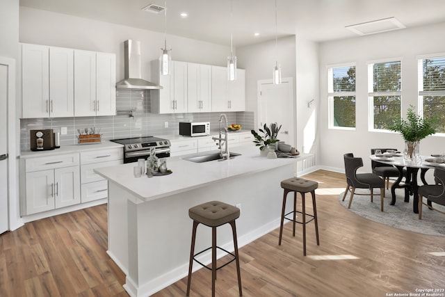 kitchen featuring wall chimney range hood, decorative light fixtures, white cabinets, and a breakfast bar