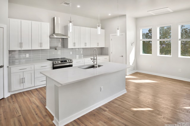 kitchen with wall chimney range hood, hardwood / wood-style floors, stainless steel range with electric cooktop, and white cabinetry