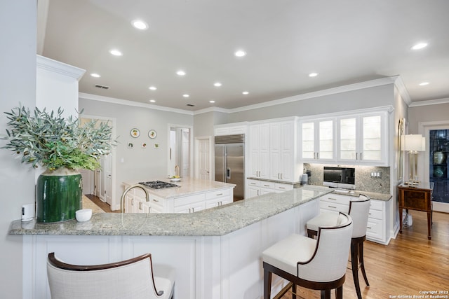 kitchen with white cabinetry, a kitchen breakfast bar, light hardwood / wood-style flooring, stainless steel built in fridge, and light stone counters