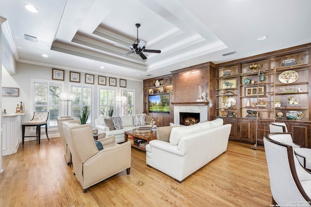 living room featuring light hardwood / wood-style floors, a fireplace, ceiling fan, and a tray ceiling