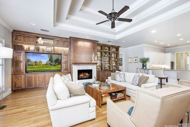 living room with a raised ceiling, crown molding, ceiling fan, and light wood-type flooring