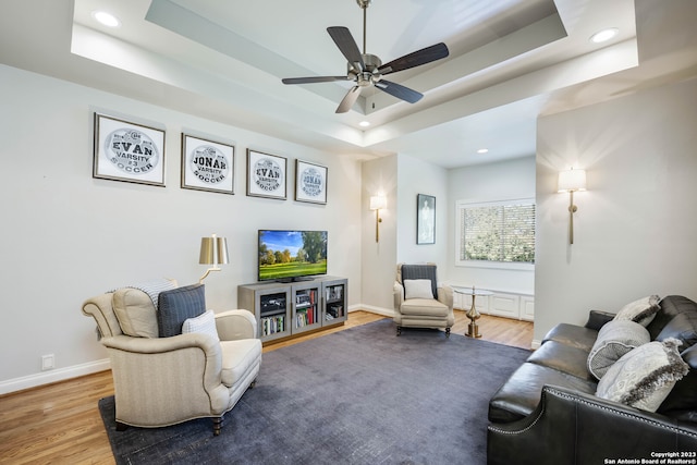 living room with a raised ceiling, light hardwood / wood-style floors, and ceiling fan