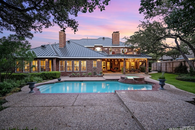 pool at dusk with a patio area and an in ground hot tub