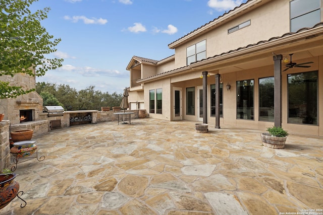 view of patio with a grill, an outdoor stone fireplace, ceiling fan, and an outdoor kitchen