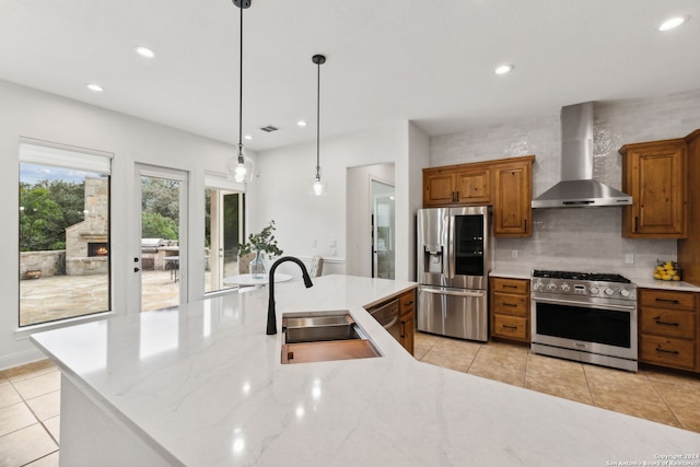 kitchen featuring light stone countertops, sink, hanging light fixtures, wall chimney range hood, and appliances with stainless steel finishes