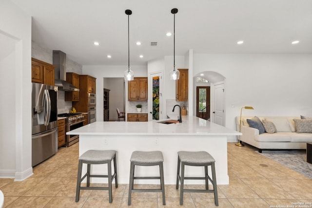 kitchen featuring sink, hanging light fixtures, stainless steel appliances, wall chimney range hood, and a breakfast bar