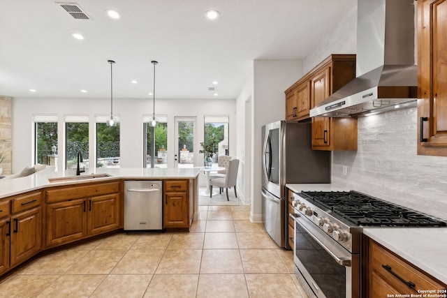 kitchen featuring a wealth of natural light, wall chimney range hood, sink, and appliances with stainless steel finishes