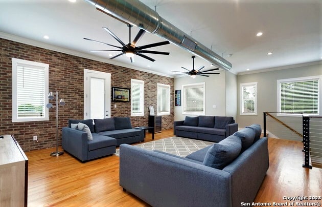 living room featuring light hardwood / wood-style flooring, brick wall, and ornamental molding