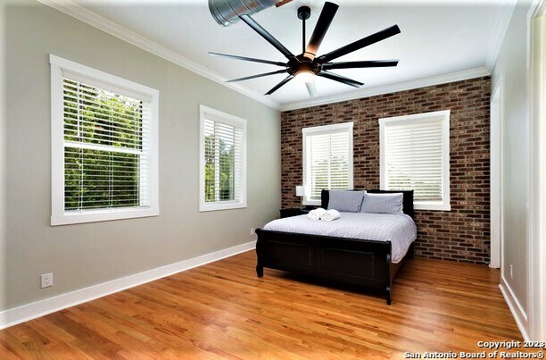 bedroom featuring light wood-type flooring, brick wall, ceiling fan, and ornamental molding