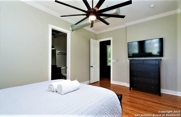 bedroom featuring a walk in closet, ceiling fan, ornamental molding, and hardwood / wood-style flooring