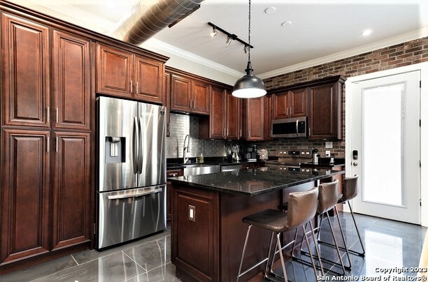 kitchen with pendant lighting, sink, dark stone countertops, a kitchen island, and stainless steel appliances