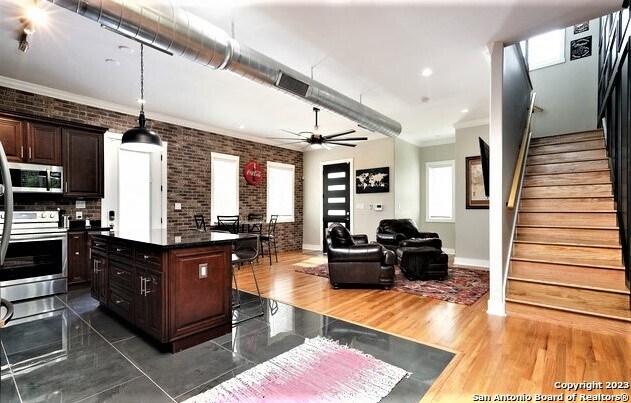 kitchen with a kitchen bar, appliances with stainless steel finishes, brick wall, dark brown cabinets, and a kitchen island