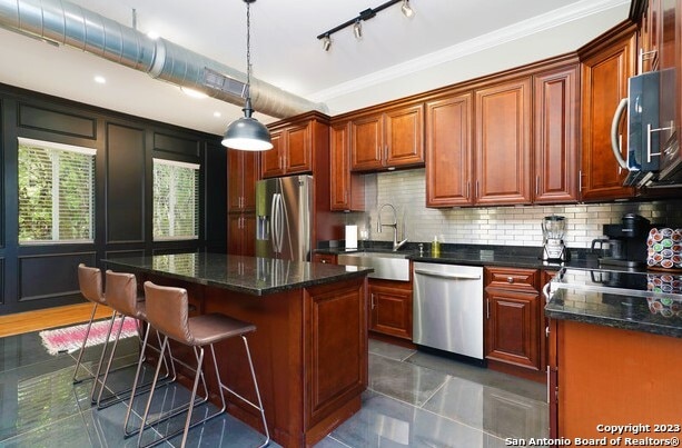 kitchen featuring appliances with stainless steel finishes, sink, a kitchen island, decorative light fixtures, and ornamental molding