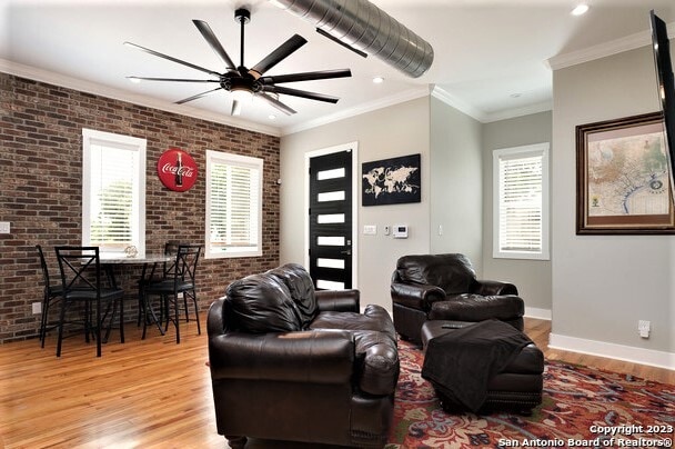 living room featuring crown molding, light hardwood / wood-style flooring, brick wall, and ceiling fan