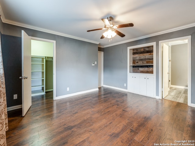 unfurnished bedroom with a closet, a walk in closet, ceiling fan, dark wood-type flooring, and crown molding