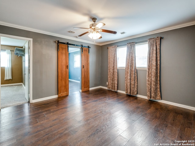 empty room with a barn door, dark wood-type flooring, ceiling fan, and crown molding