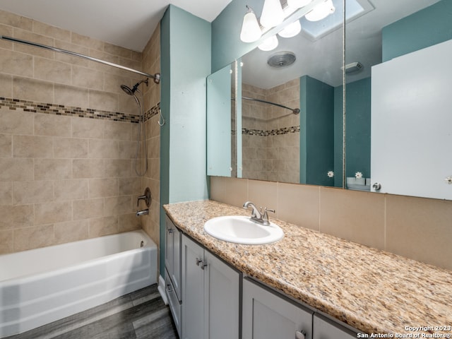 bathroom featuring tiled shower / bath combo, large vanity, tasteful backsplash, and wood-type flooring