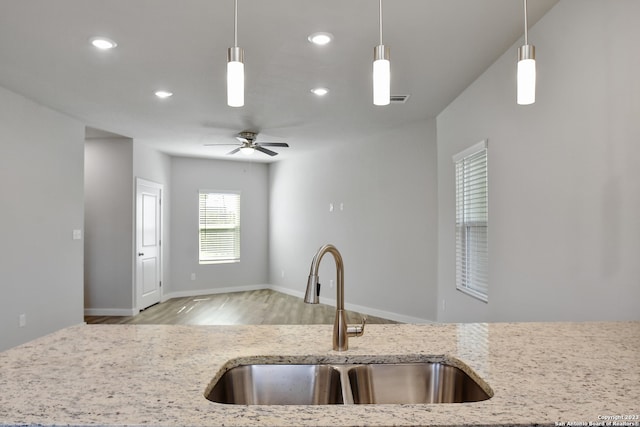 kitchen with pendant lighting, light stone countertops, ceiling fan, light hardwood / wood-style flooring, and sink