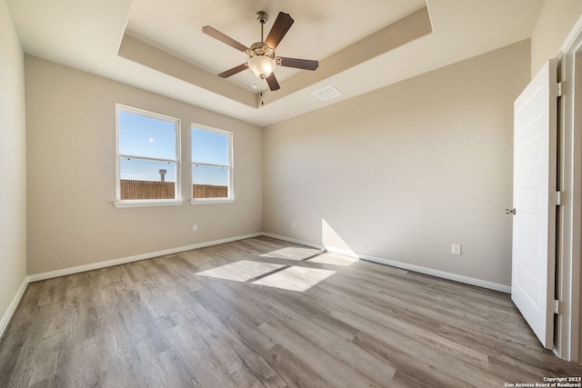 unfurnished room featuring a raised ceiling, ceiling fan, and light wood-type flooring