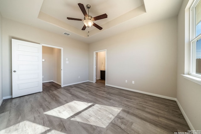 unfurnished bedroom with light wood-type flooring, ensuite bathroom, a raised ceiling, and ceiling fan