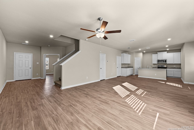 unfurnished living room with ceiling fan, sink, and light hardwood / wood-style flooring