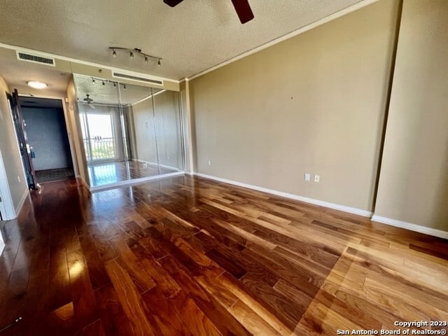 unfurnished bedroom featuring rail lighting, a textured ceiling, hardwood / wood-style flooring, and a barn door