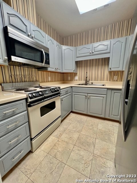 kitchen featuring gray cabinetry, stainless steel appliances, light tile floors, and sink