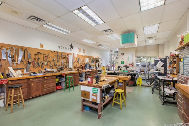 miscellaneous room featuring concrete flooring, a drop ceiling, and a workshop area