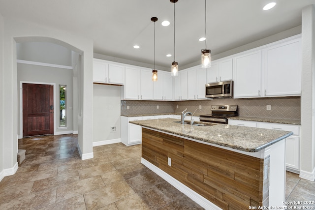 kitchen featuring stainless steel appliances, a center island with sink, white cabinets, hanging light fixtures, and sink