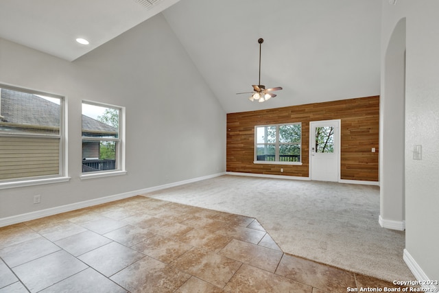 spare room with wooden walls, high vaulted ceiling, ceiling fan, and light colored carpet