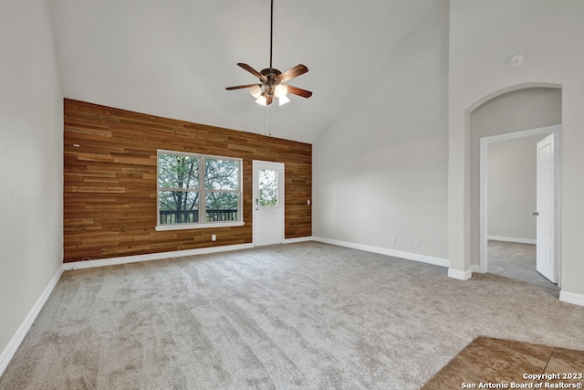 empty room with light colored carpet, wood walls, ceiling fan, and high vaulted ceiling