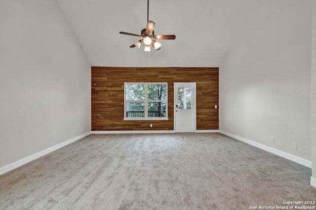 carpeted spare room with high vaulted ceiling, wooden walls, and ceiling fan