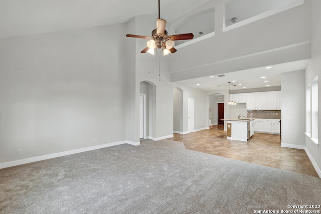 unfurnished living room with high vaulted ceiling, light carpet, and ceiling fan