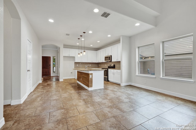 kitchen with appliances with stainless steel finishes, pendant lighting, tasteful backsplash, light tile floors, and a kitchen island with sink