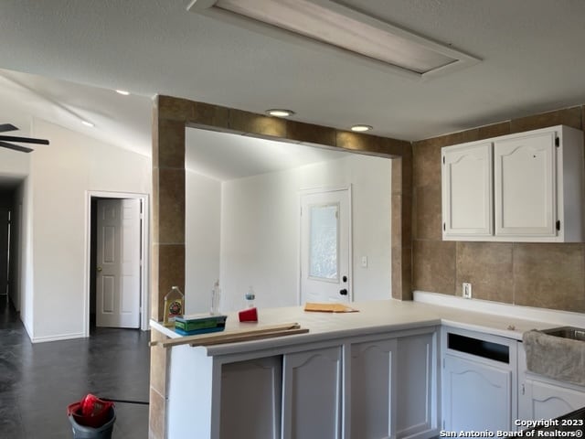 kitchen with ceiling fan, kitchen peninsula, white cabinetry, lofted ceiling, and tile walls