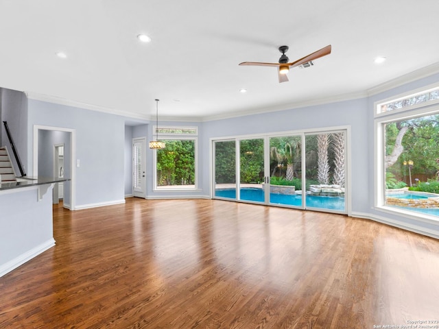 unfurnished living room with dark hardwood / wood-style floors, crown molding, ceiling fan with notable chandelier, and a wealth of natural light