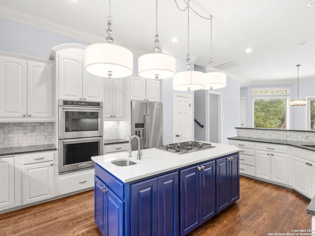 kitchen with pendant lighting, blue cabinets, appliances with stainless steel finishes, backsplash, and sink