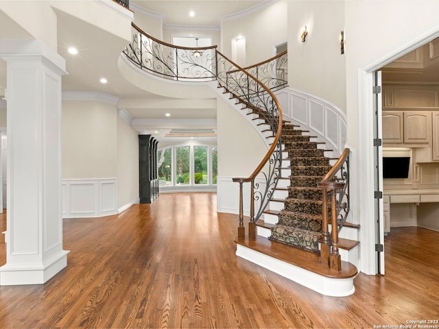 foyer with a high ceiling, hardwood / wood-style floors, crown molding, and ornate columns