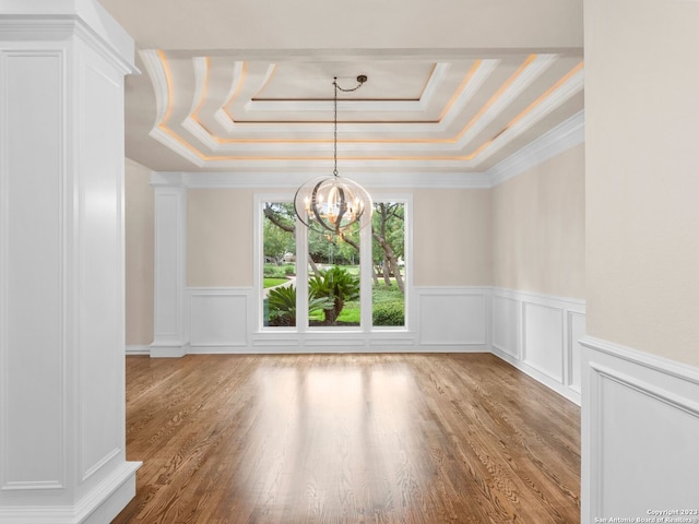 spare room with an inviting chandelier, a raised ceiling, ornamental molding, and light hardwood / wood-style floors