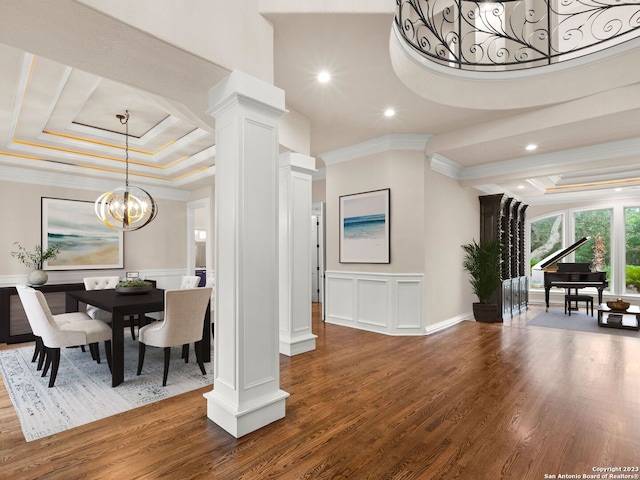 dining space featuring a tray ceiling, dark wood-type flooring, an inviting chandelier, crown molding, and ornate columns